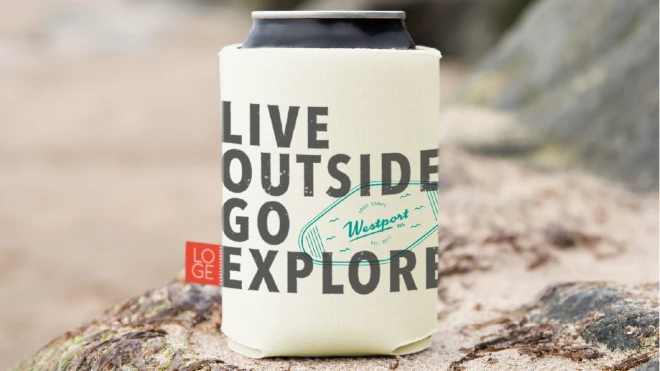 A can cooler with the text "LIVE OUTSIDE GO EXPLORE", featuring the LOGE Camps logo and a graphic of a keychain tag with the text "Westport, WA". The cooler is placed on a rock, with a blurred background.